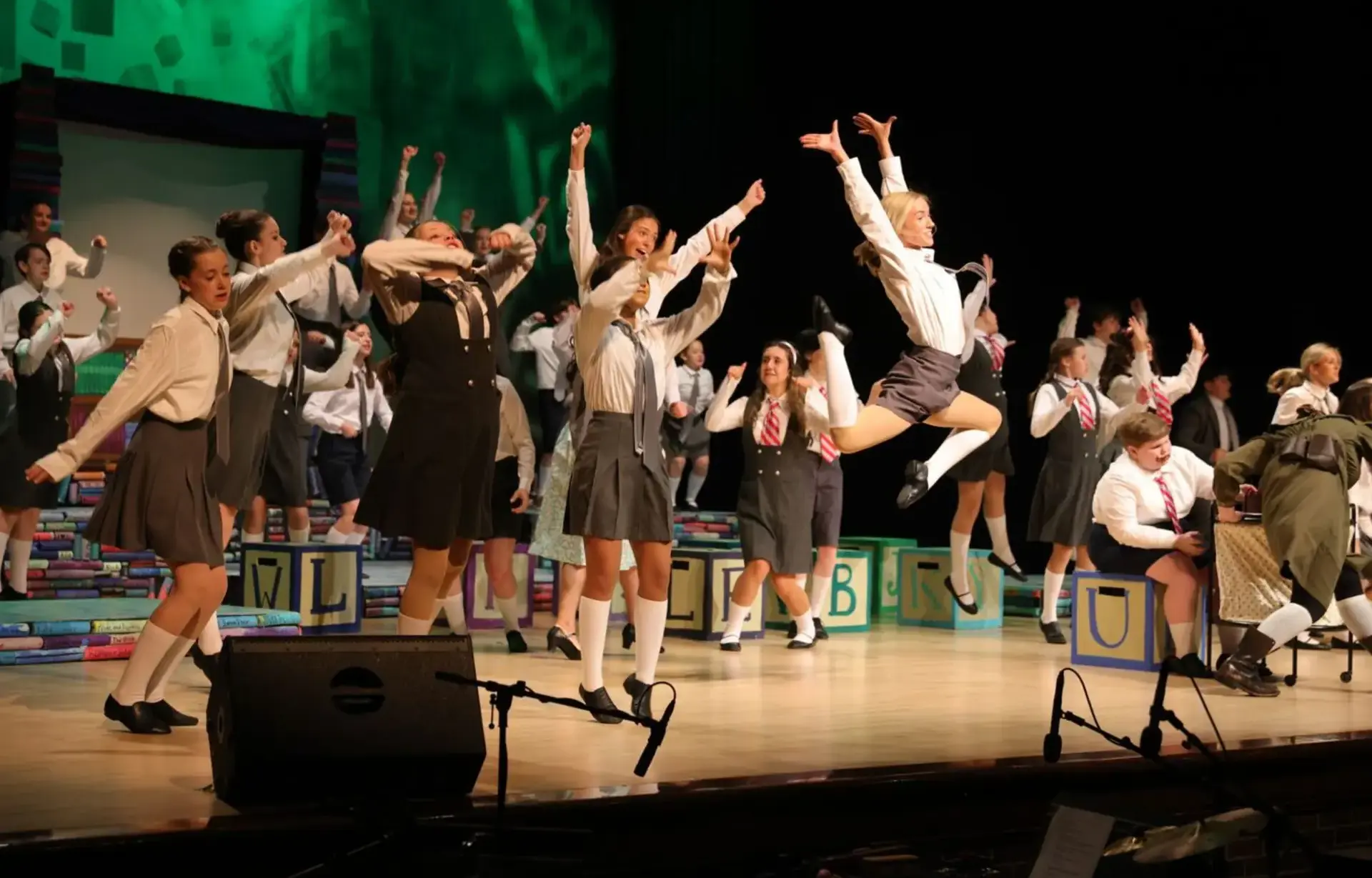 Students perform an energetic musical theater number on stage.