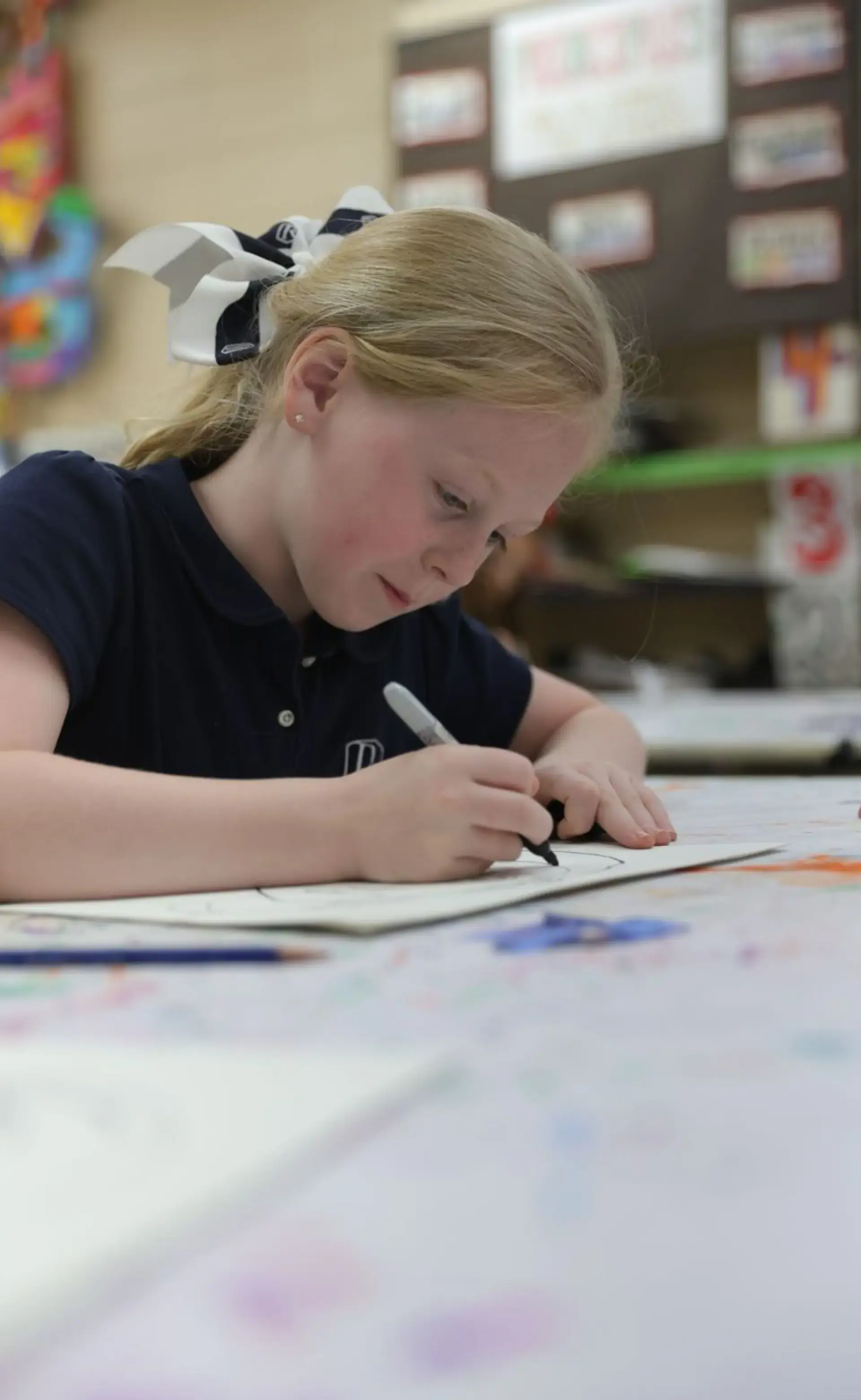 Student concentrating while drawing at a classroom table.