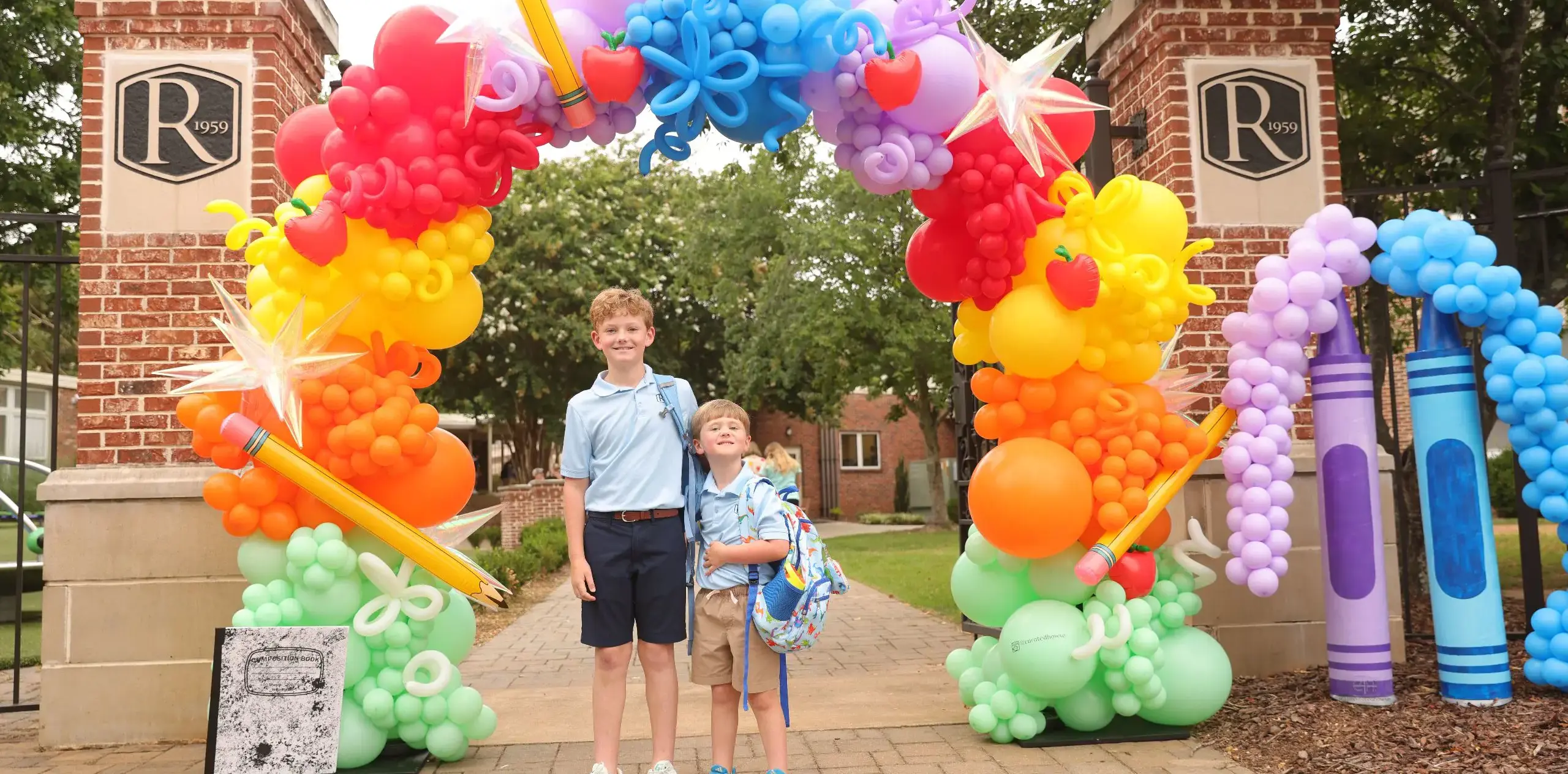 Two students standing beneath a colourful back-to-school balloon arch at a school entrance