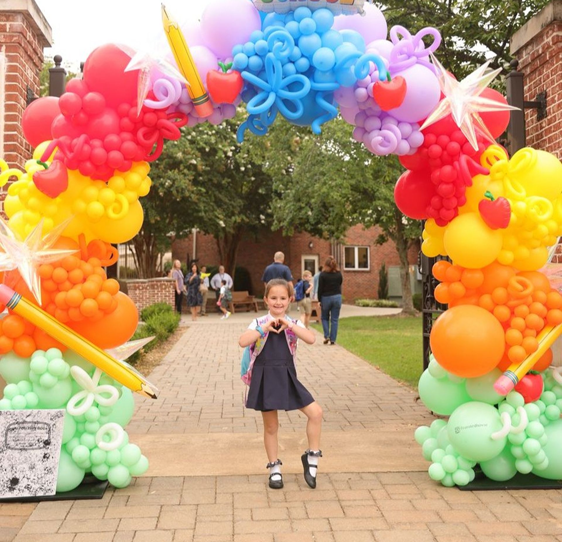 Young student poses under a colorful balloon arch on the first day of school.