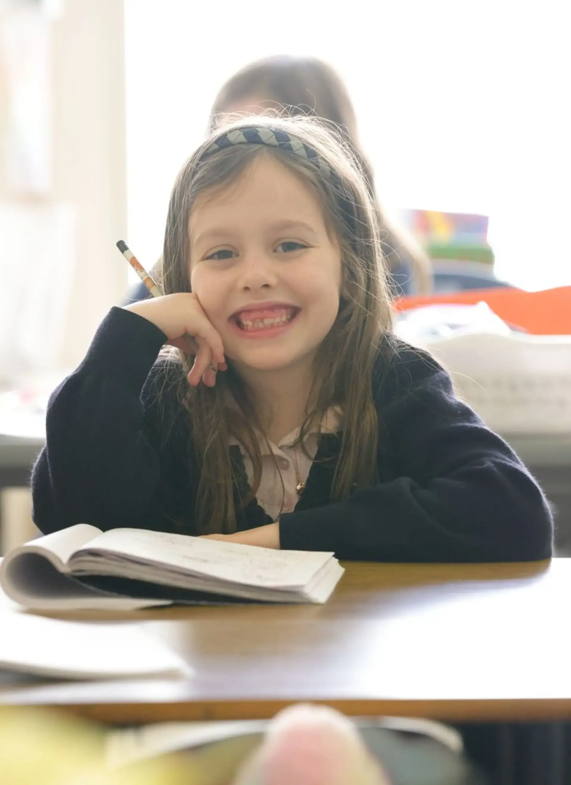 Smiling student sits at a desk with an open notebook in class.