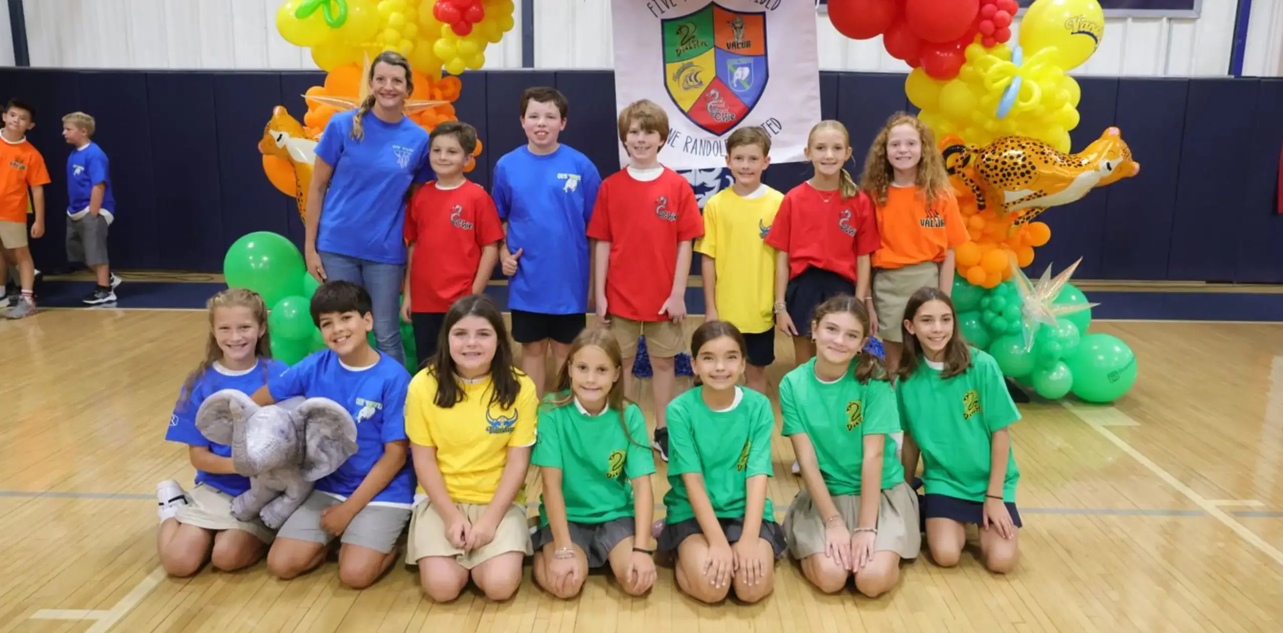Students and teacher pose in colorful team shirts at a school spirit event.