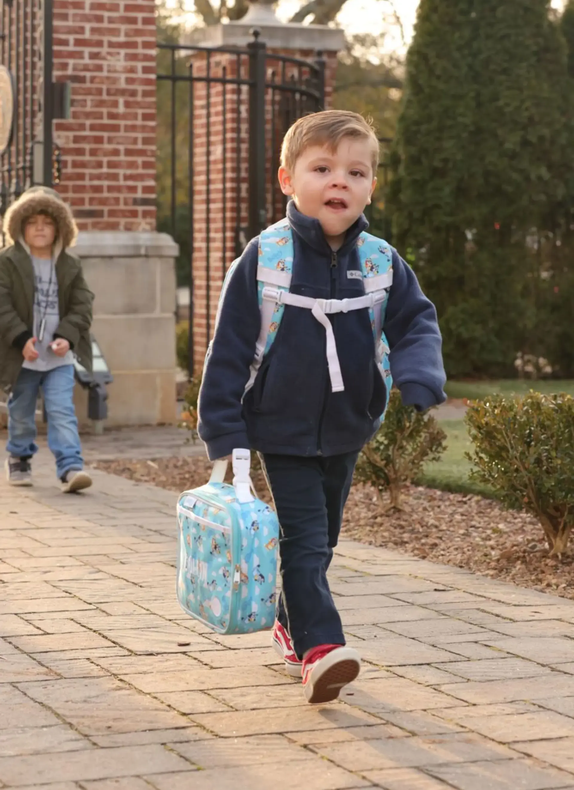 Young student walks to school carrying a backpack and lunch bag.
