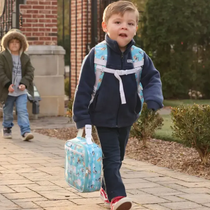 Young student walks to school carrying a backpack and lunch bag.