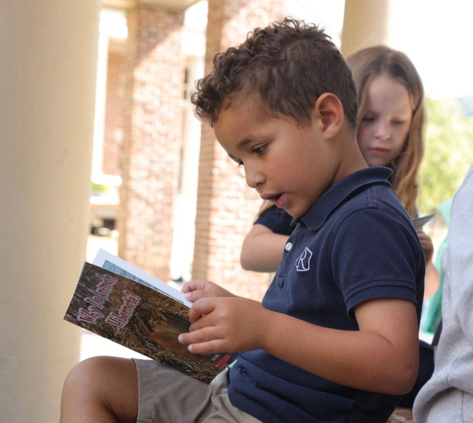 lower school students reading a book outdoors