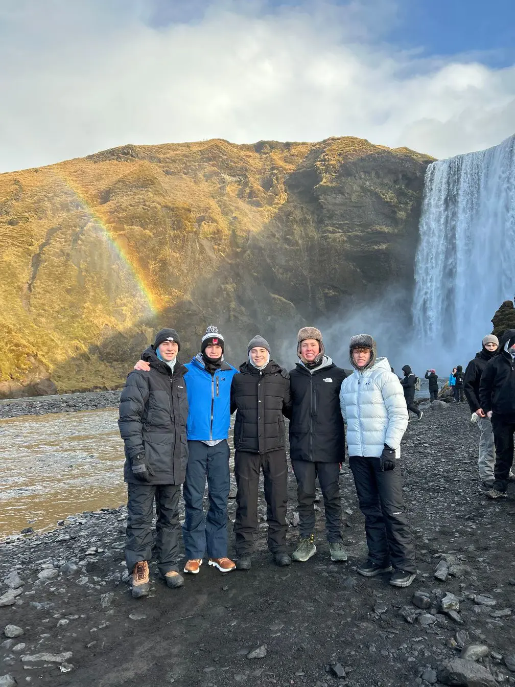 Students explore Iceland, with a rainbow and a waterfall in the background, on their interim trip. 