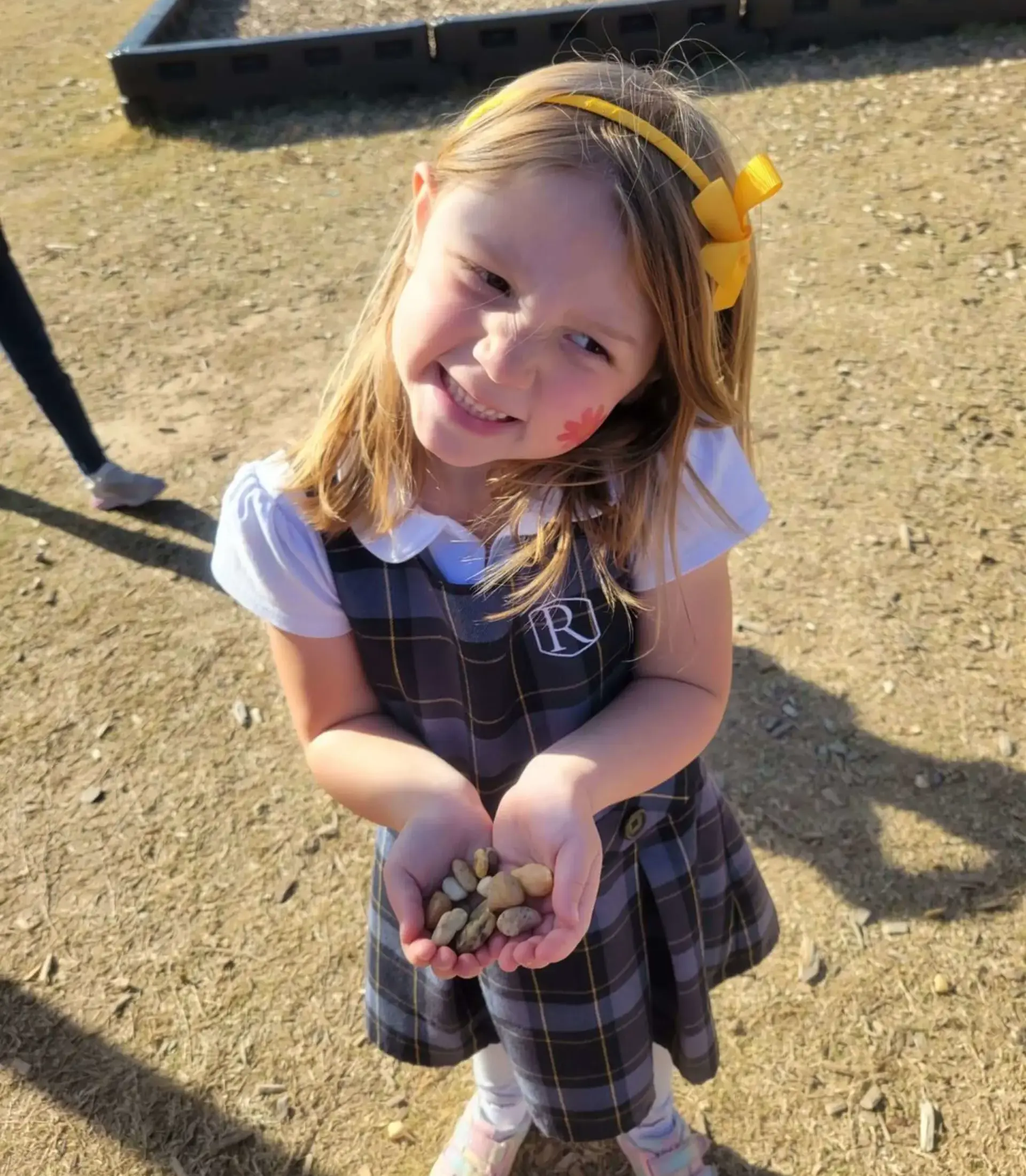 Young student smiling outdoors while holding a collection of small rocks.