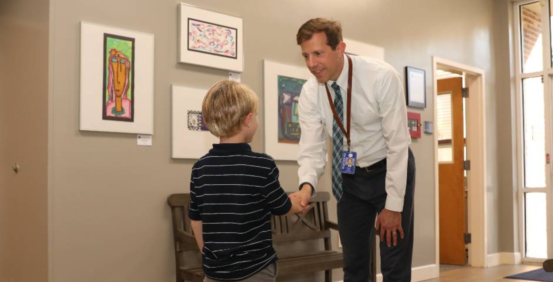 School administrator greeting a young student in a hallway.