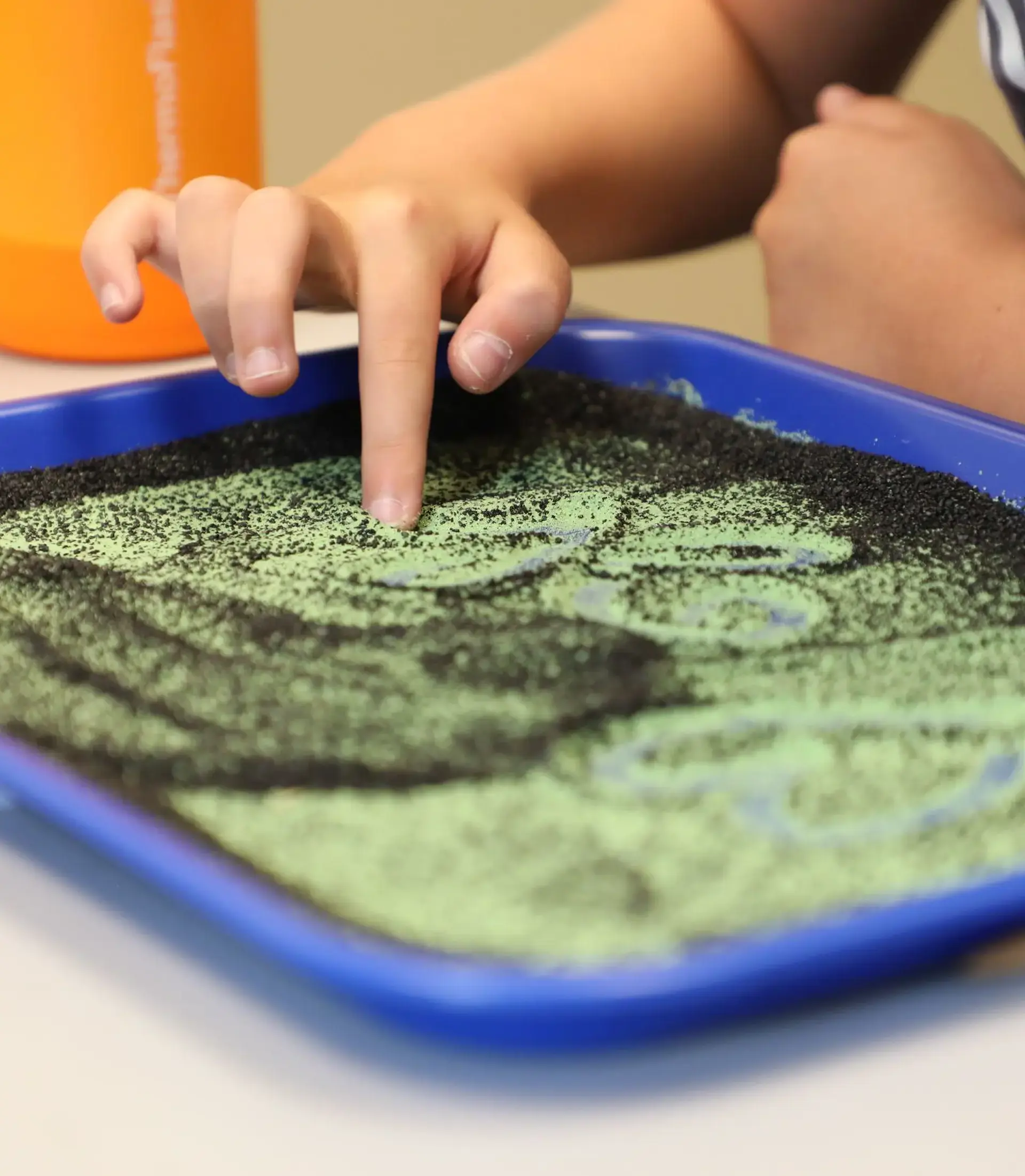 Child tracing shapes with a finger in a sensory sand tray.
