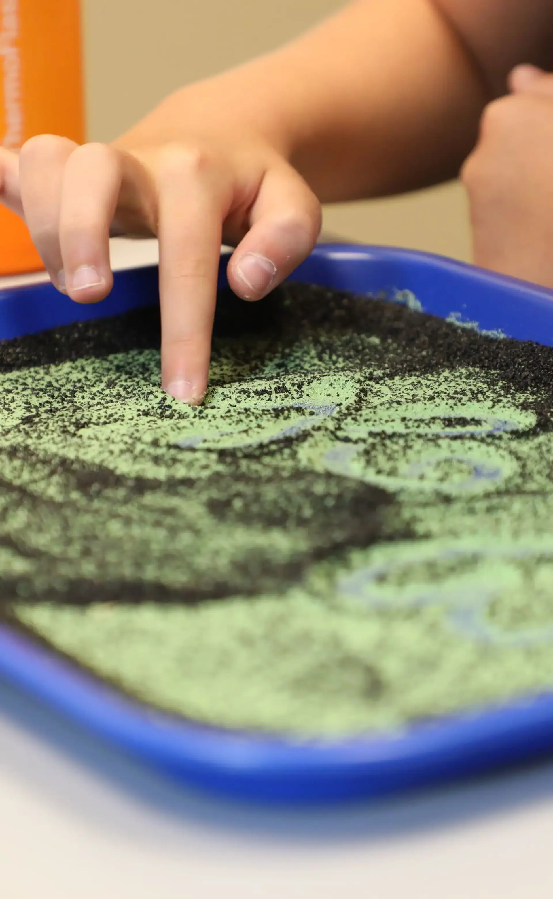 Child tracing shapes with a finger in a sensory sand tray.