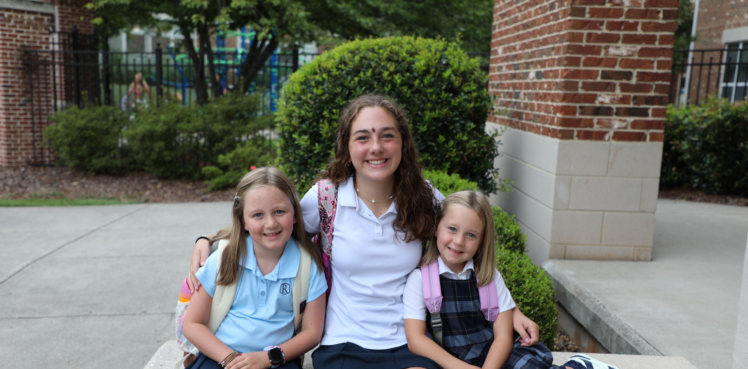 Three students smiling together outside on campus.