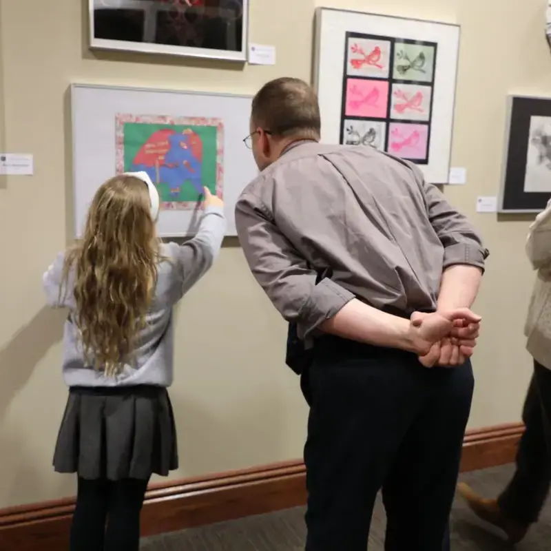 Student and adult view and discuss artwork at a school art exhibit.