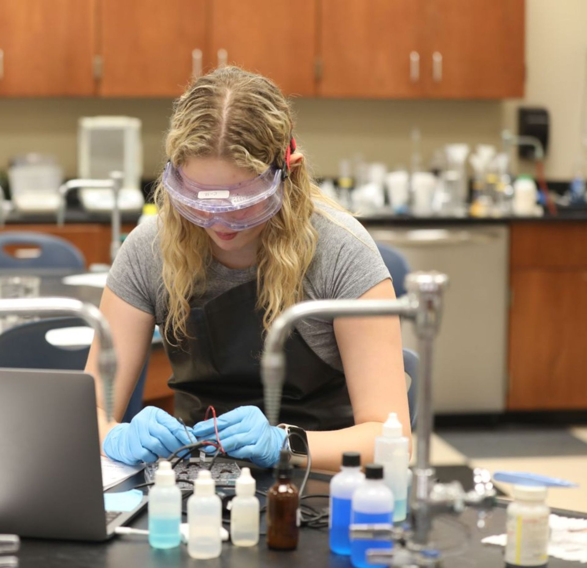 Student wearing safety goggles and gloves while conducting a science lab experiment.