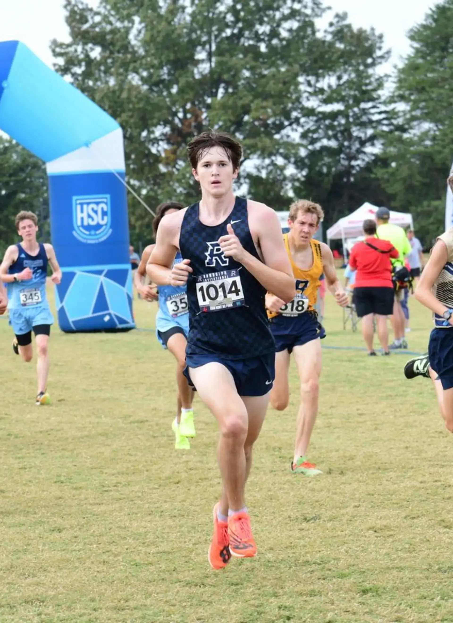 Student runner leads a cross-country race across a grassy course during a school meet.