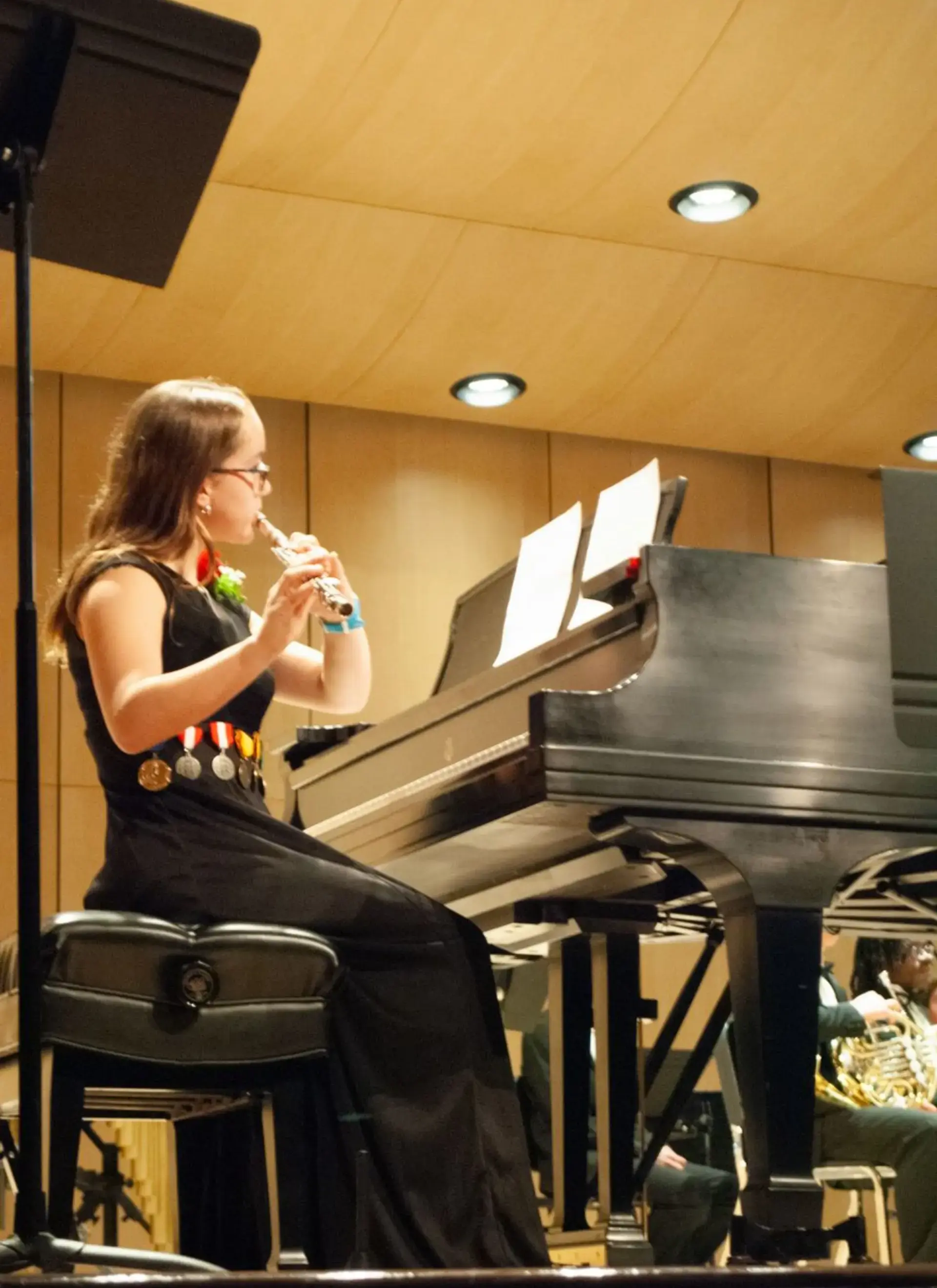 Student performs a flute solo beside a grand piano during a school music recital.