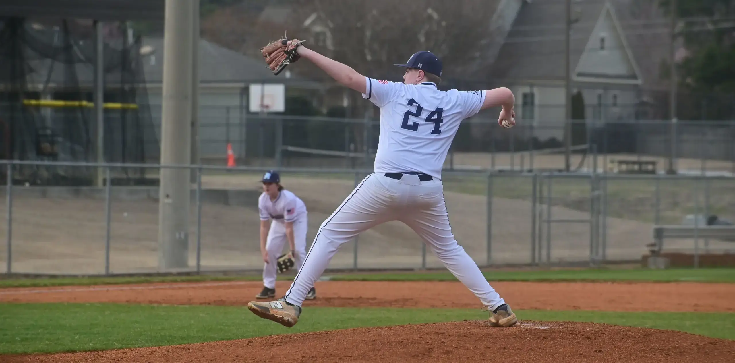 Baseball player pitching during a game while a teammate prepares in the field.