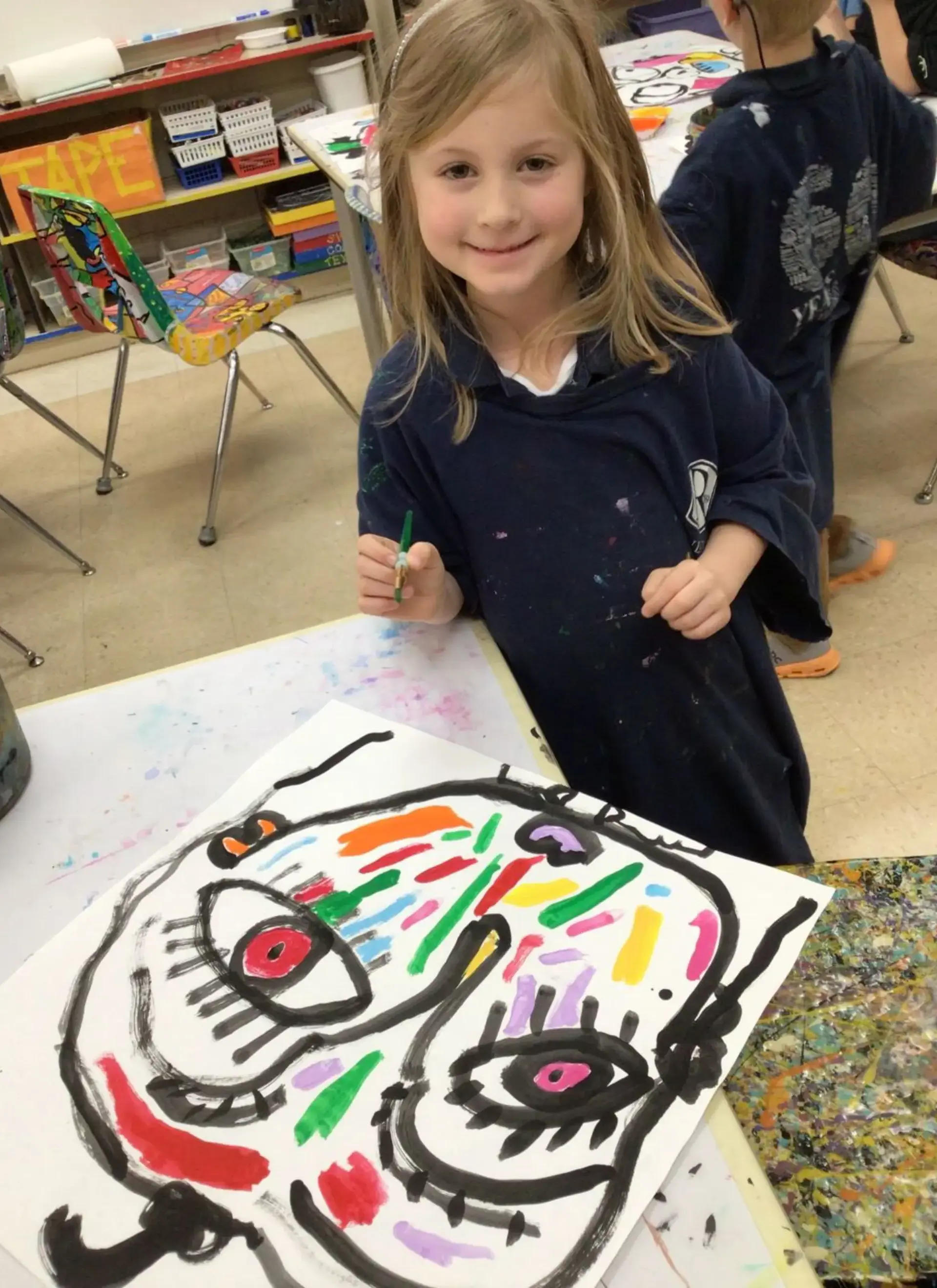 Young student proudly displays a colorful portrait painting during an art class.