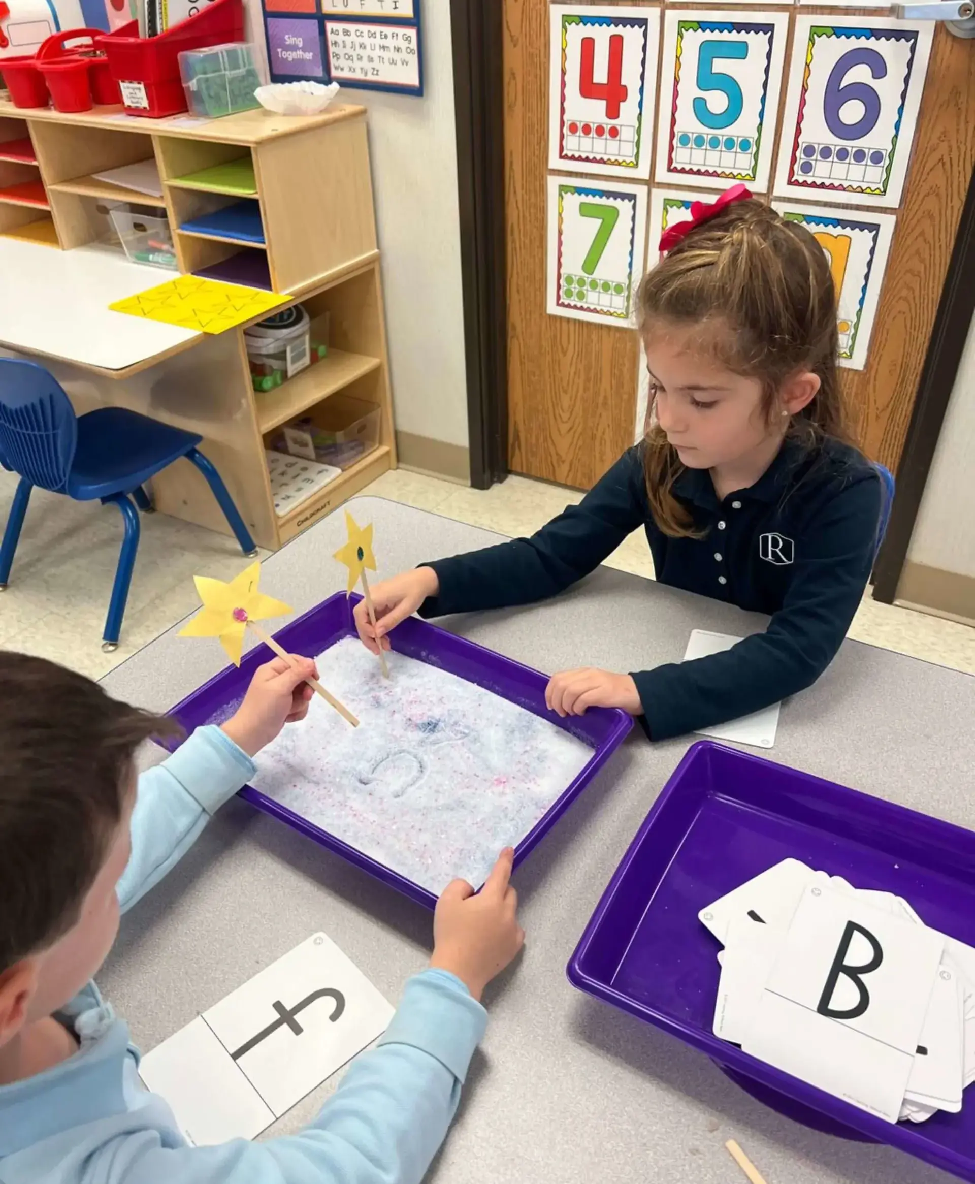 Young students practicing letters in a sensory learning activity.