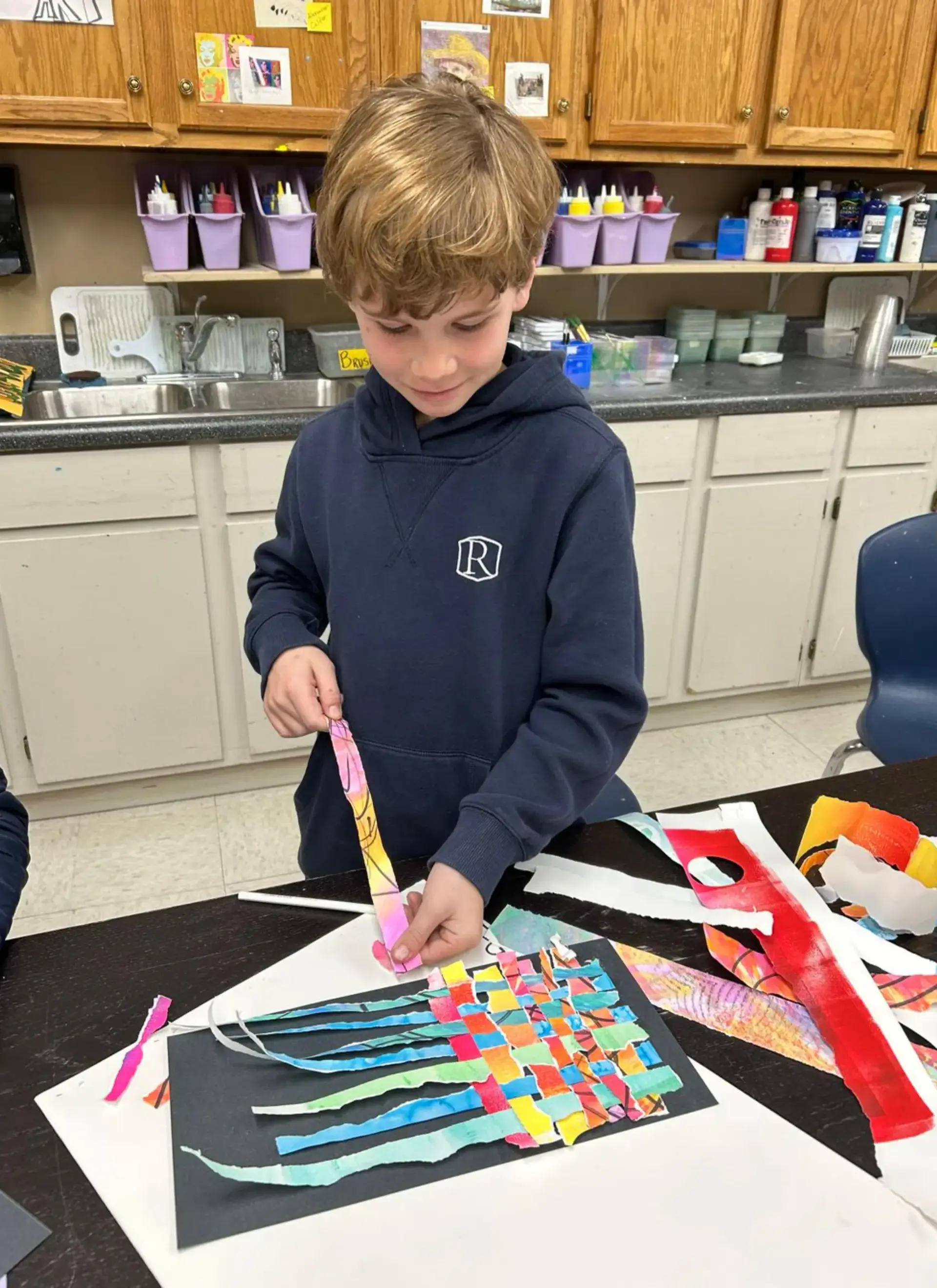 Student creates a colorful woven paper collage during an art class project.