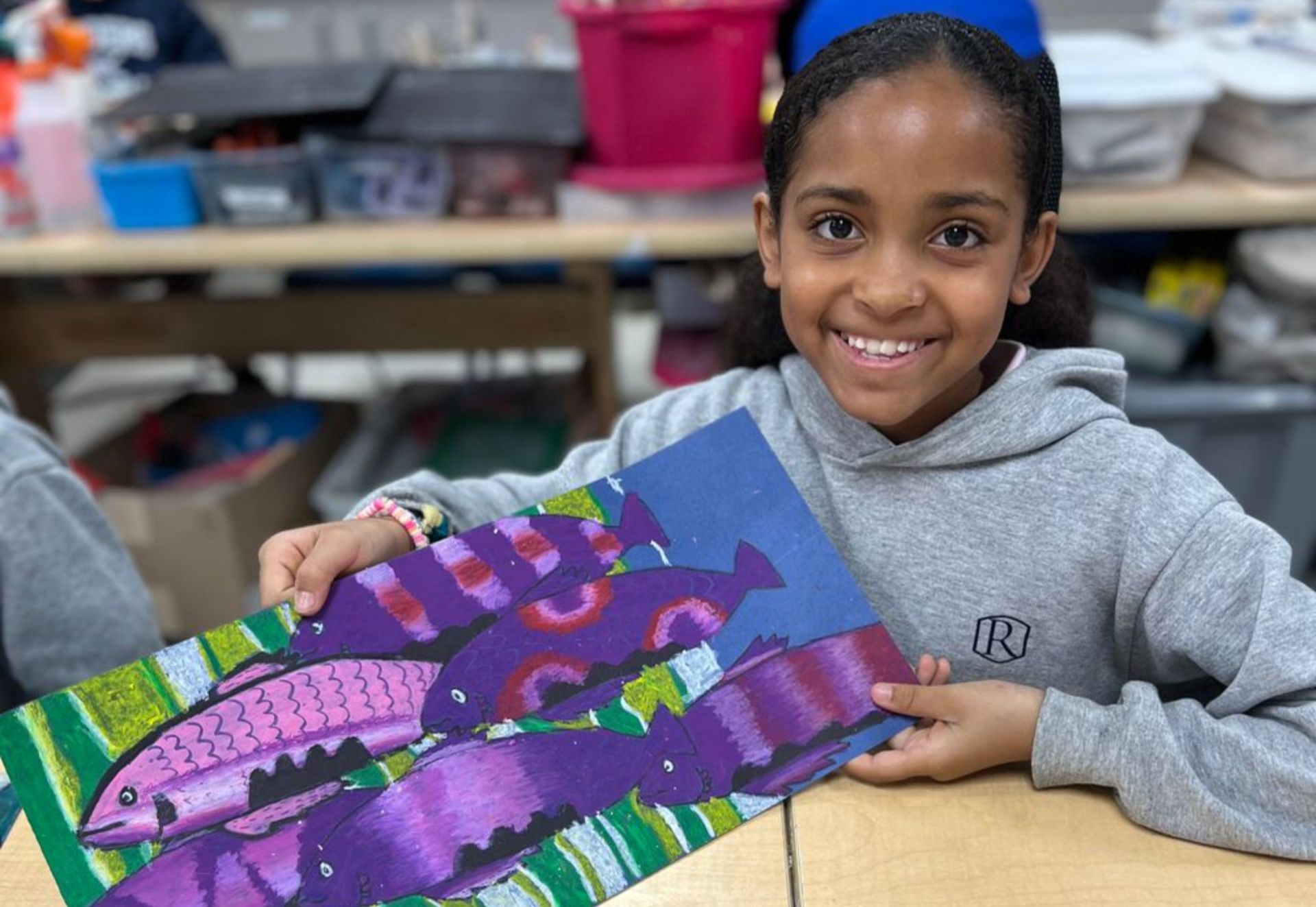 Student proudly displays a colorful fish painting in art class.