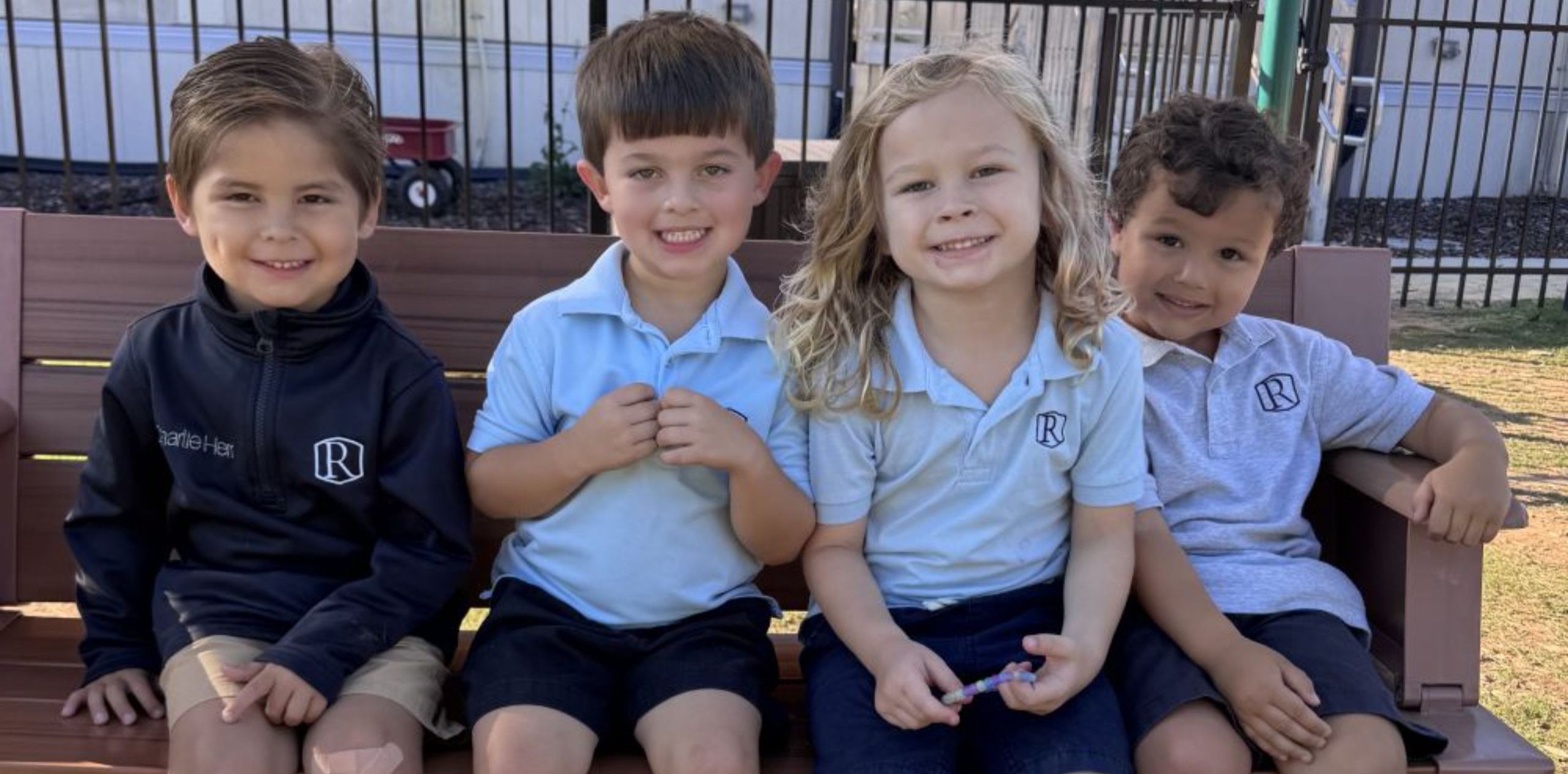 group of lower school students sitting on a bench smiling