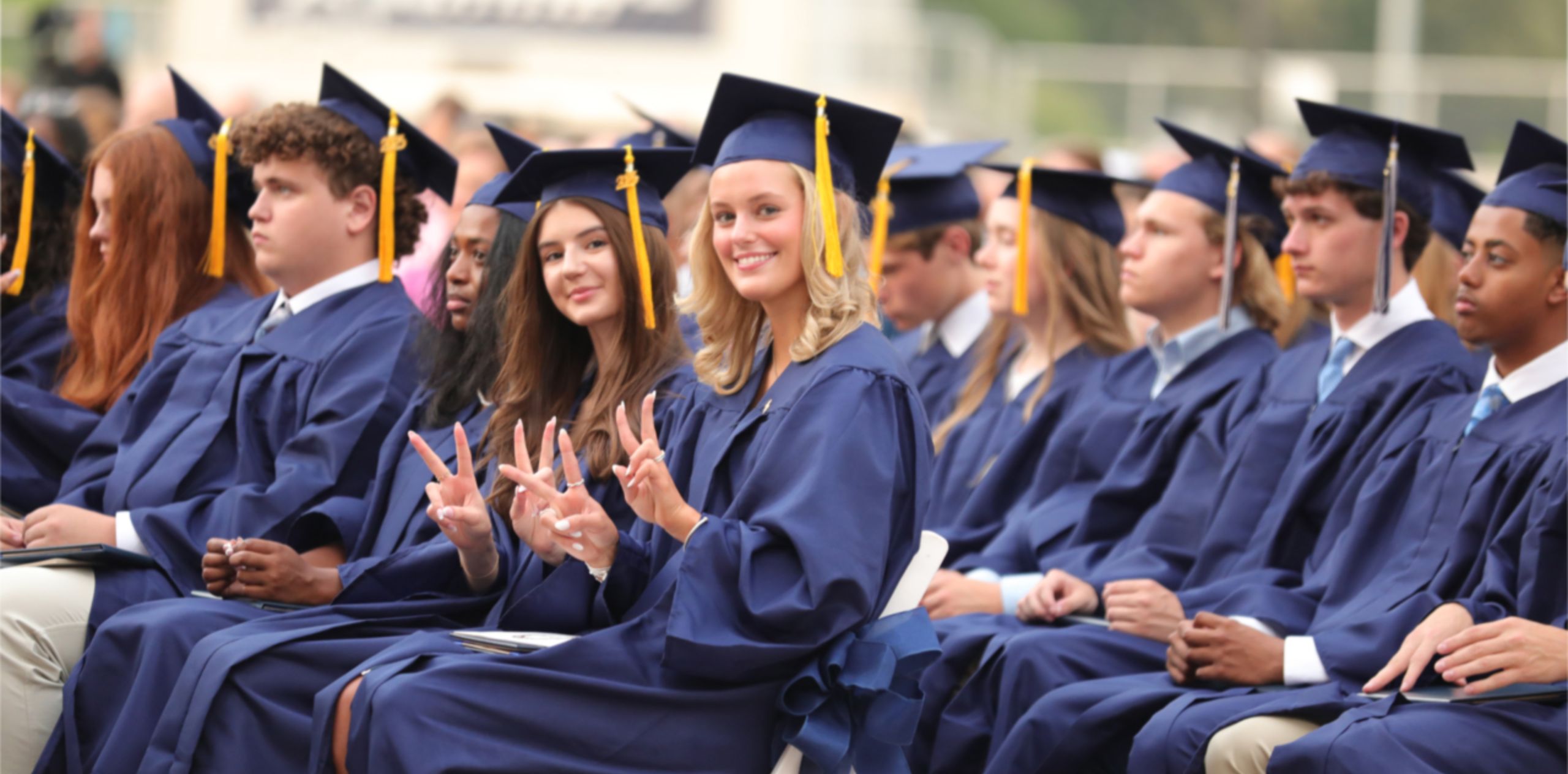 Two Randolph School seniors in graduation attire smile and give peace signs on commencement day, celebrating their achievement together.