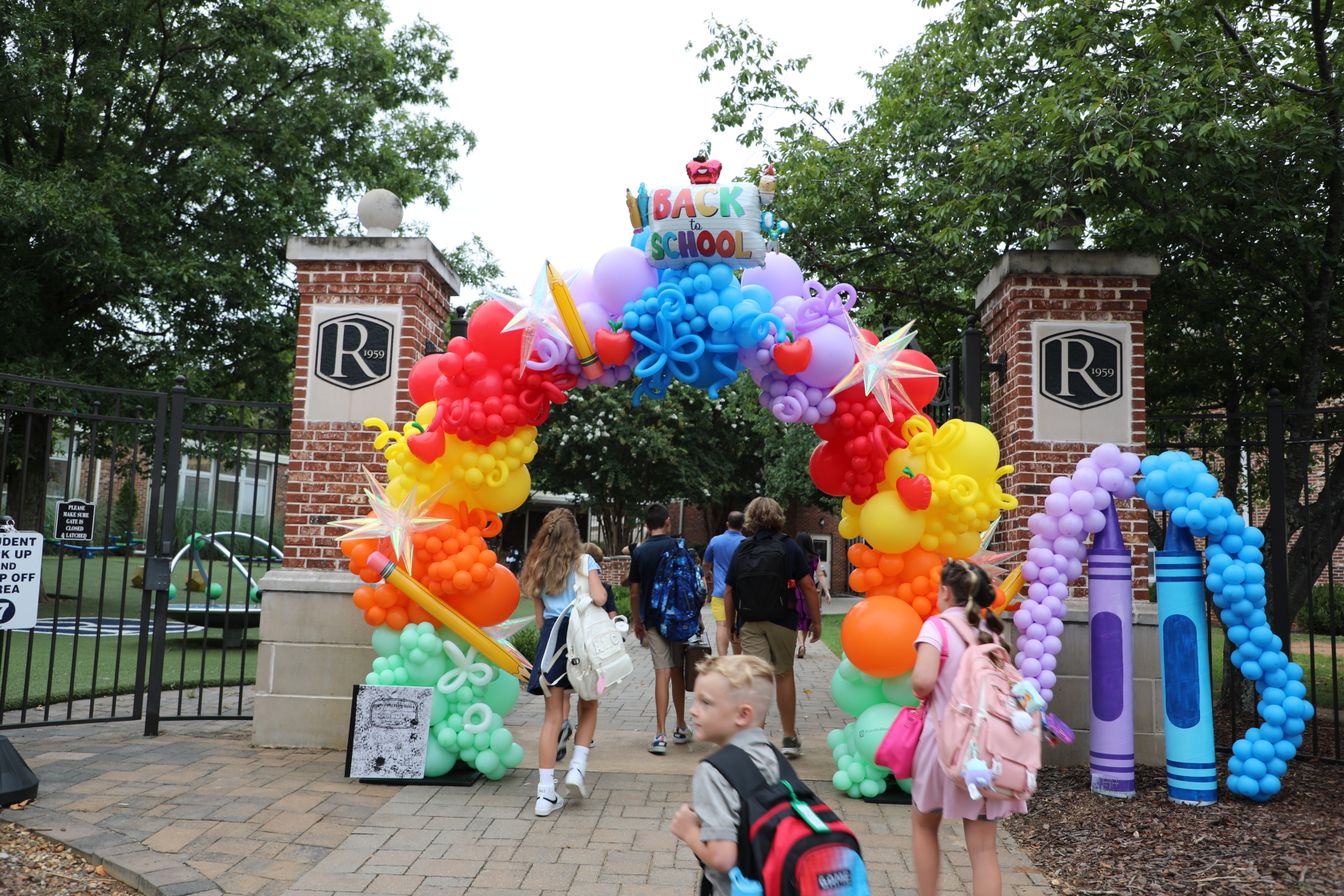Students walking through a colorful back-to-school balloon arch at Randolph school entrance.