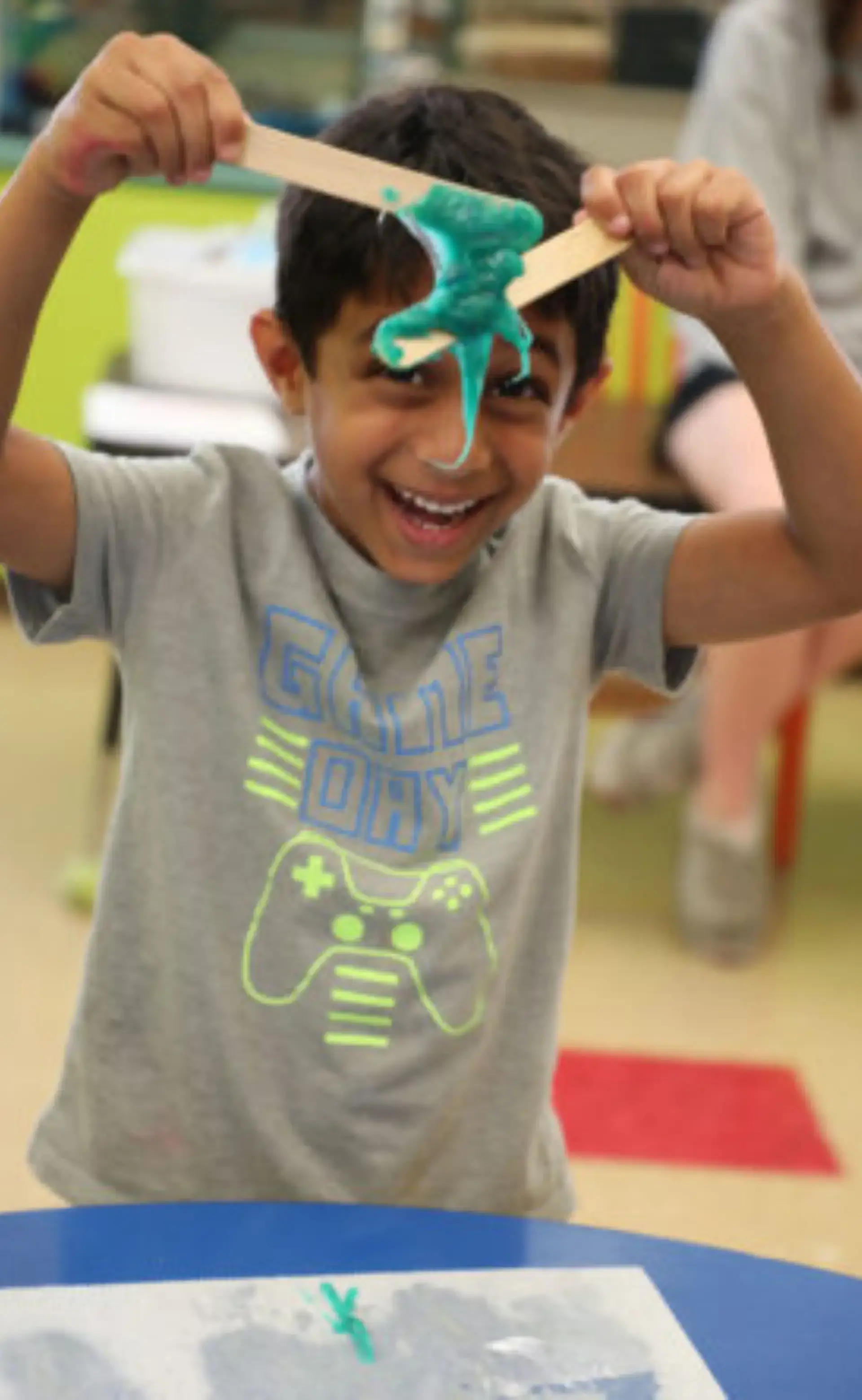 Smiling child holding up stretchy blue slime during a hands-on classroom activity.